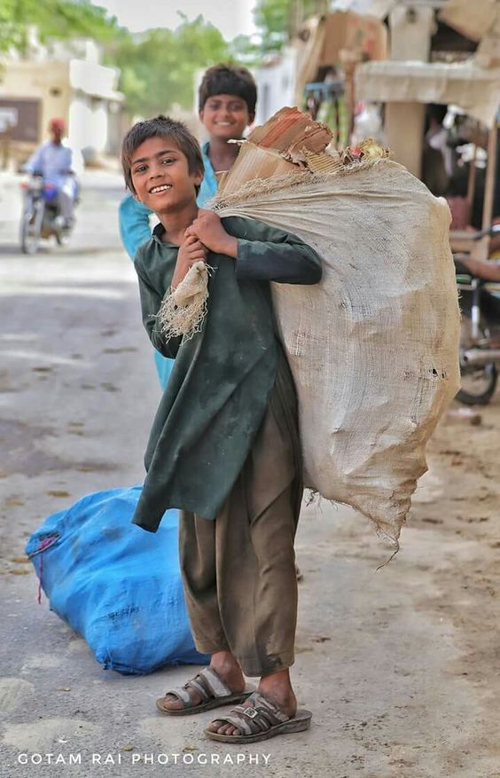 a young boy carrying a large bag on his back down the street with two other people in the background