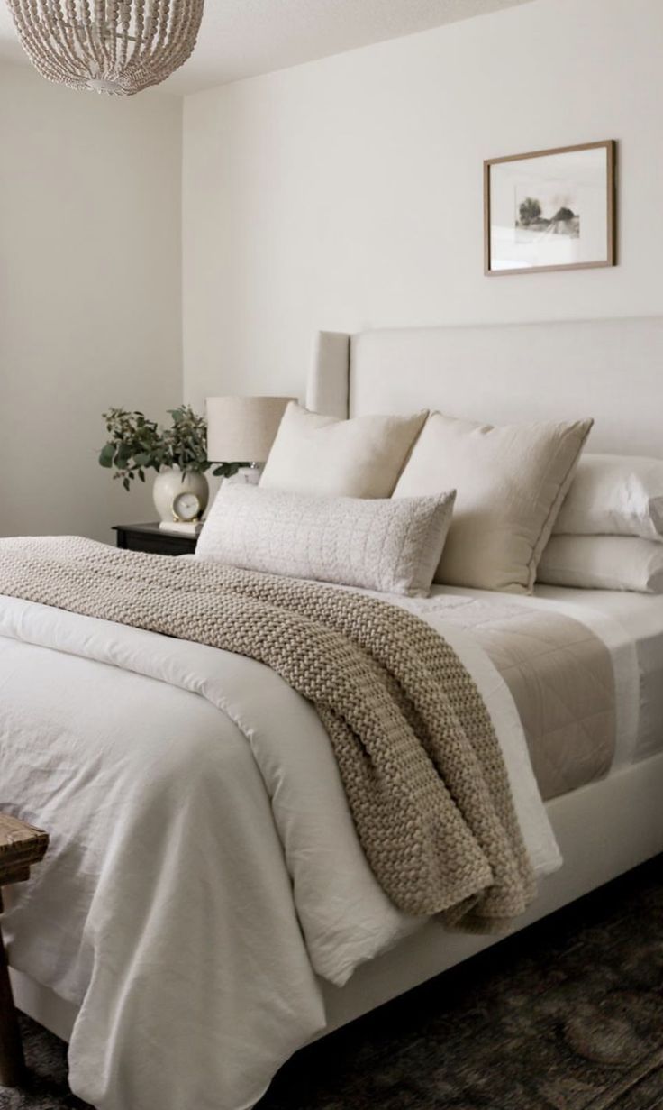 a bed with white linens and pillows in a bedroom next to a lamp on the wall