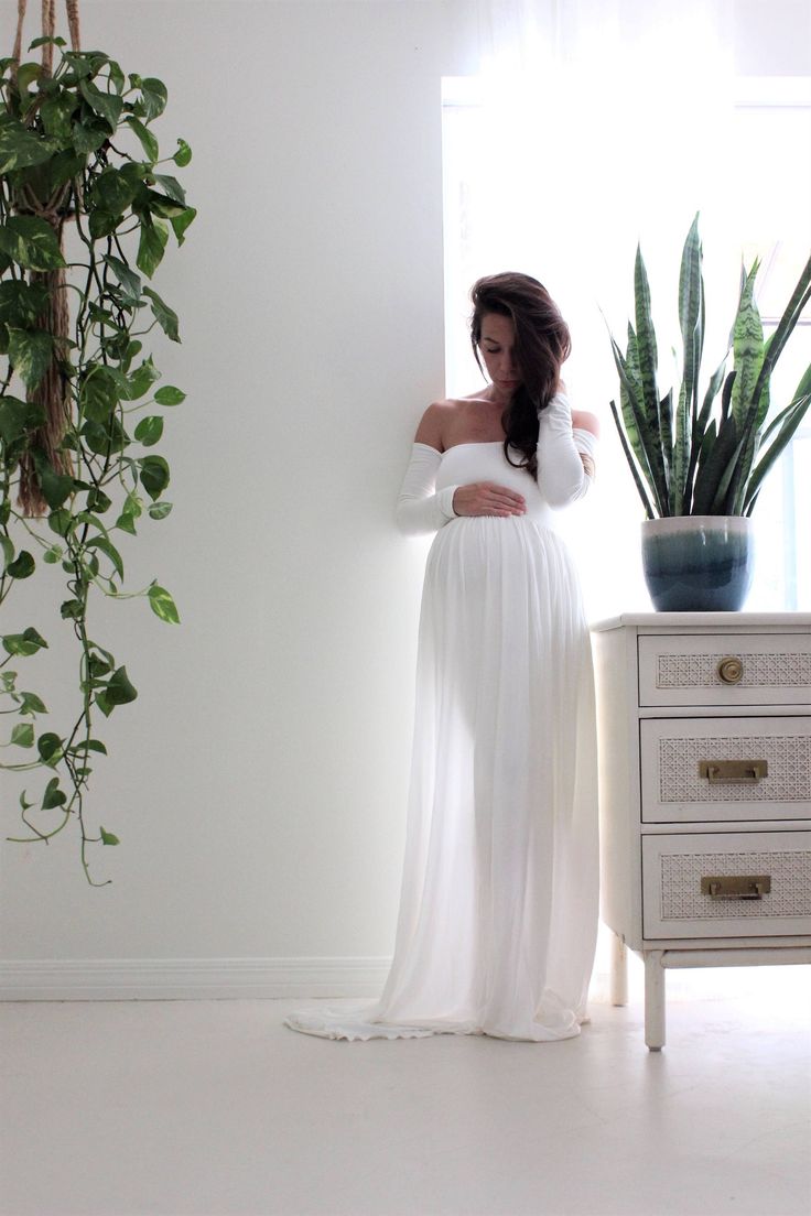 a woman in a white dress standing next to a potted plant on a dresser