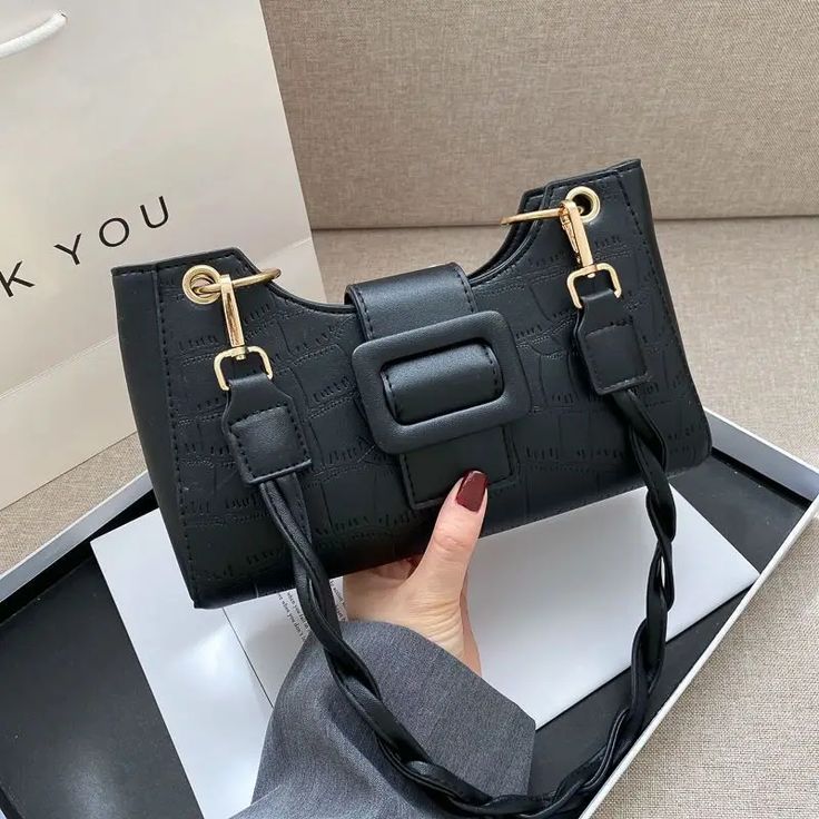 a woman holding a black handbag in her right hand and the other one has a gold buckle on it