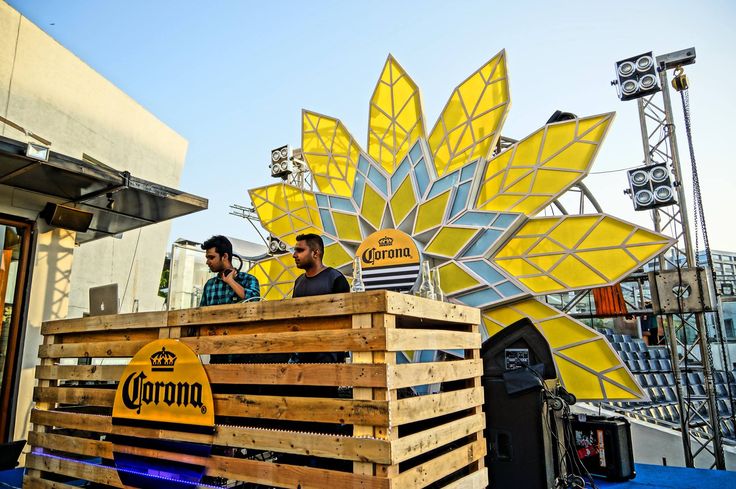 two men standing on top of a wooden crate in front of a large yellow flower