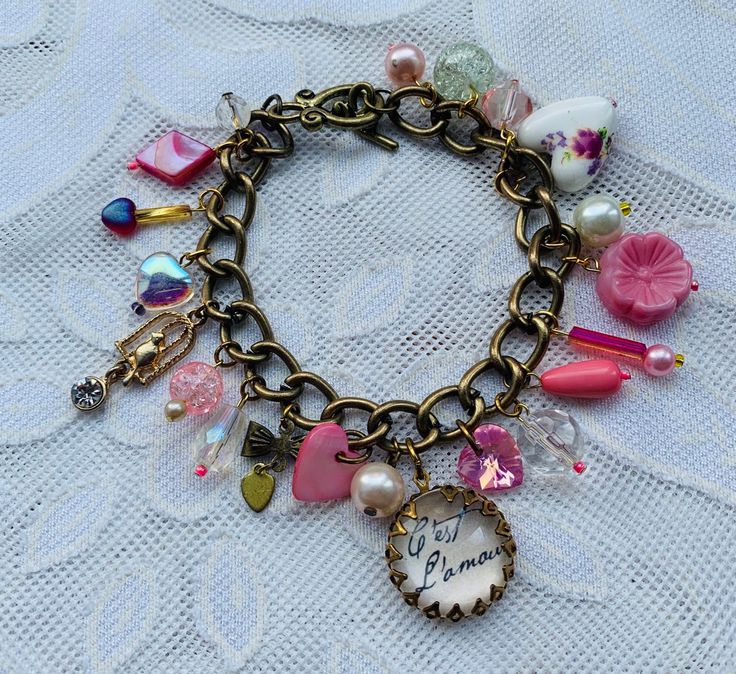 Vintage C'est l'amour charm bracelet French inspired one of a kind design bracelet upon a wide loop antique brass chain with toggle clasp With 21 charms including: C'est l'amour vintage charm, swarovski pink heart, birdcage charm, porcelain floral heart charm, pink engraved glass flower, faux pearls, crackle glass beads, faceted beads and more Chain is approx 19cm length Bracelets Design, Design Bracelet, Bracelet Design, Crackle Glass, Love Hearts, French Inspired, Brass Chain, Faceted Bead, Charm Bracelets