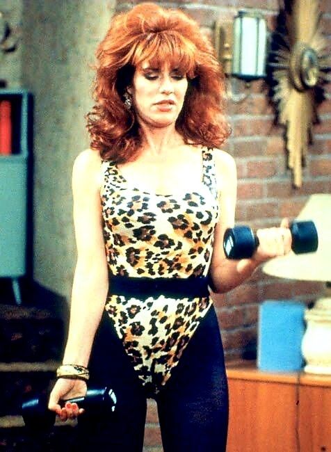 a woman with red hair in a leopard print bodysuit holding two dumbbells