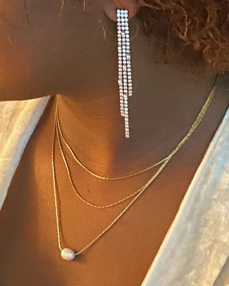 the back of a woman's head wearing three layered necklaces with pearls on them