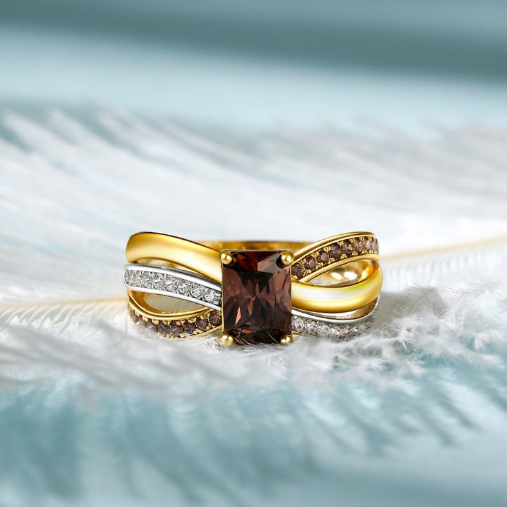 two gold rings with brown and white diamonds on them sitting on top of an ostrich feather