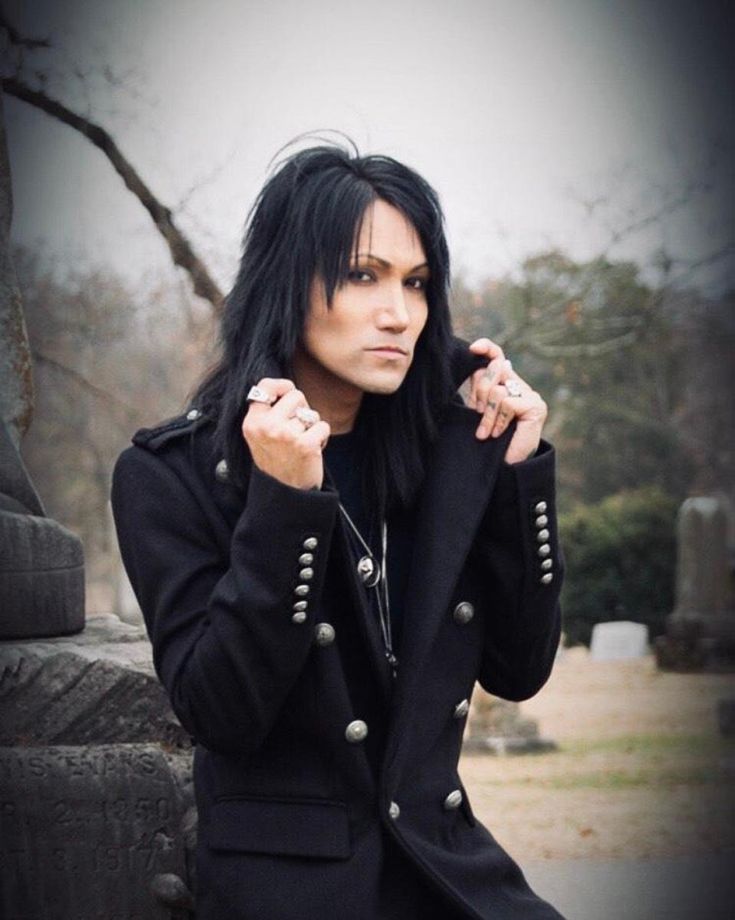 a woman with black hair and piercings sitting on a stone wall in a cemetery