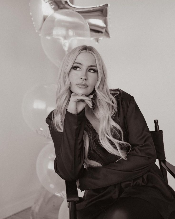 a black and white photo of a woman sitting in a chair with balloons behind her