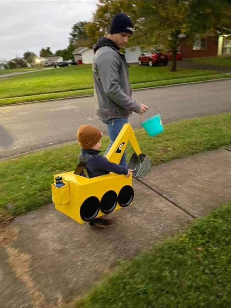 a young boy riding on the back of a yellow toy car next to a man