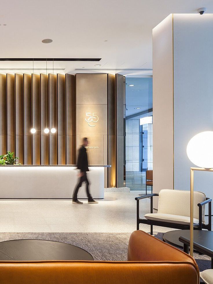 a man walking in front of a reception area with chairs and lamps on the walls