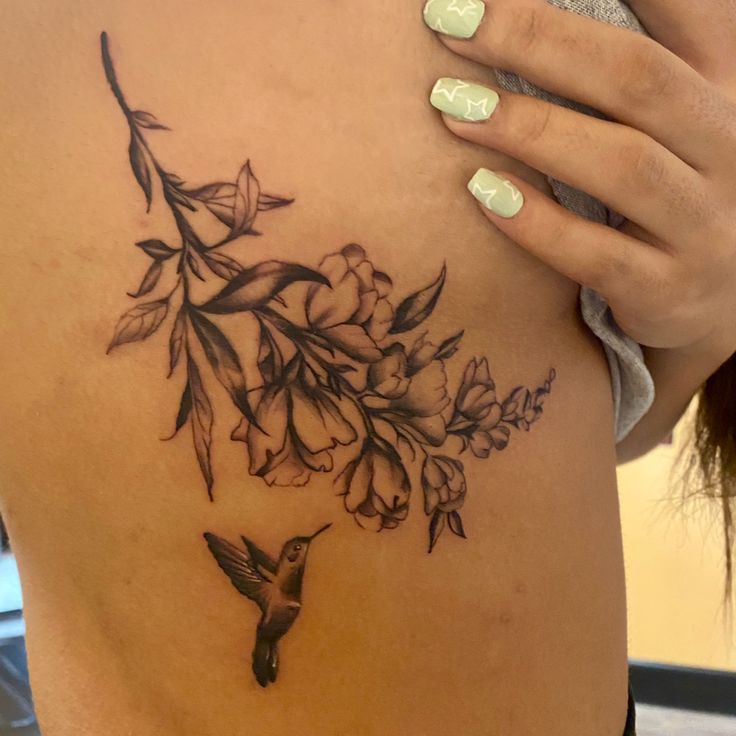 a woman's stomach with a hummingbird and flowers tattoo on her back side