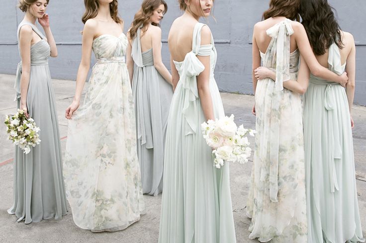 a group of women in dresses standing next to each other on the sidewalk with their backs turned