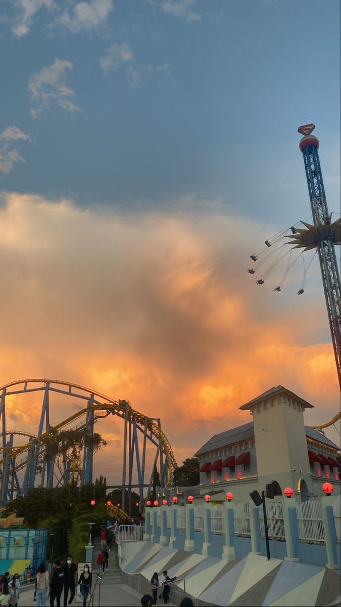 an amusement park at sunset with roller coasters in the foreground and people walking around