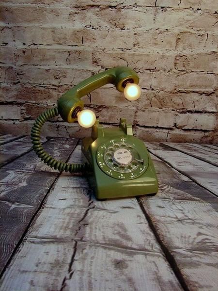 an old green telephone sitting on top of a wooden table next to a brick wall