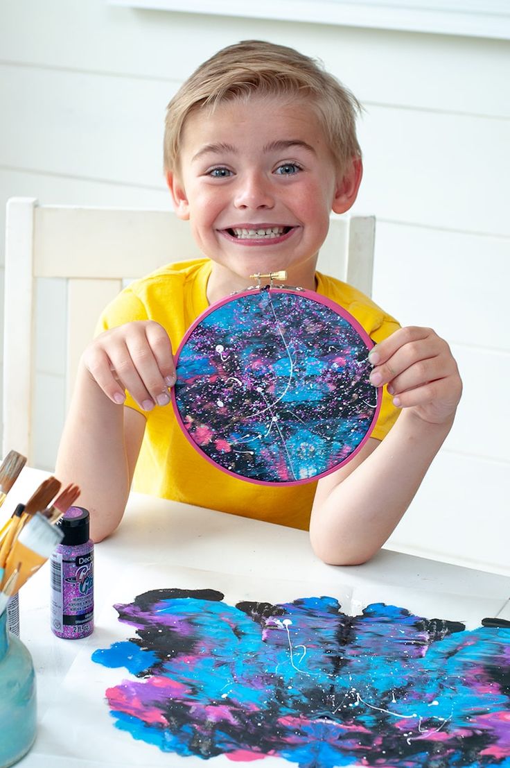 a young boy sitting at a table holding up a painting