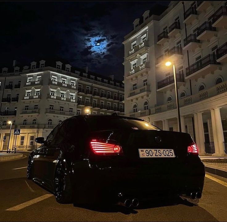 a black car parked in front of a building at night with the moon behind it