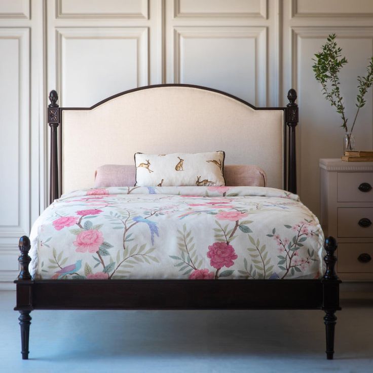 a bed with pink flowers on it in a bedroom next to a dresser and drawers