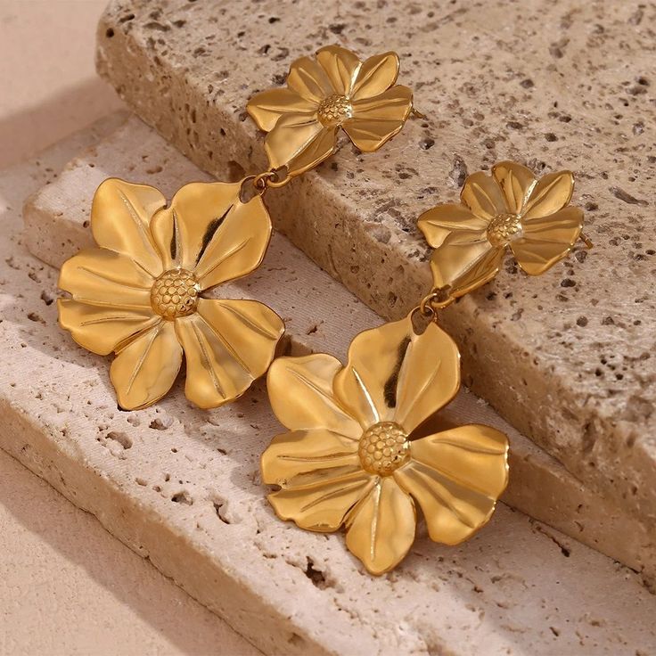 Transform any outfit with these Gold Flower Drop Earrings! These unique earrings feature delicate flowers that add a touch of femininity, and the dangle design creates movement and elegance. Elevate your style and make a statement with these gorgeous earrings. DETAILS & SIZE Sold as a pair Finish: 18K gold plate Material: Stainless Steel Measurements: 2.5"x1.5" Weight: 19.3 grams Comes with friction earring backs Waterproof, tarnish-resistant, and nickel free Shop Earrings to curate your ear stack! Flower Earrings Dangle, Gold Flower Earrings, Enchanted Jewelry, Stud Fashion, Flower Drop Earrings, Earring Stand, Long Drop Earrings, Gold Flower, Delicate Flower