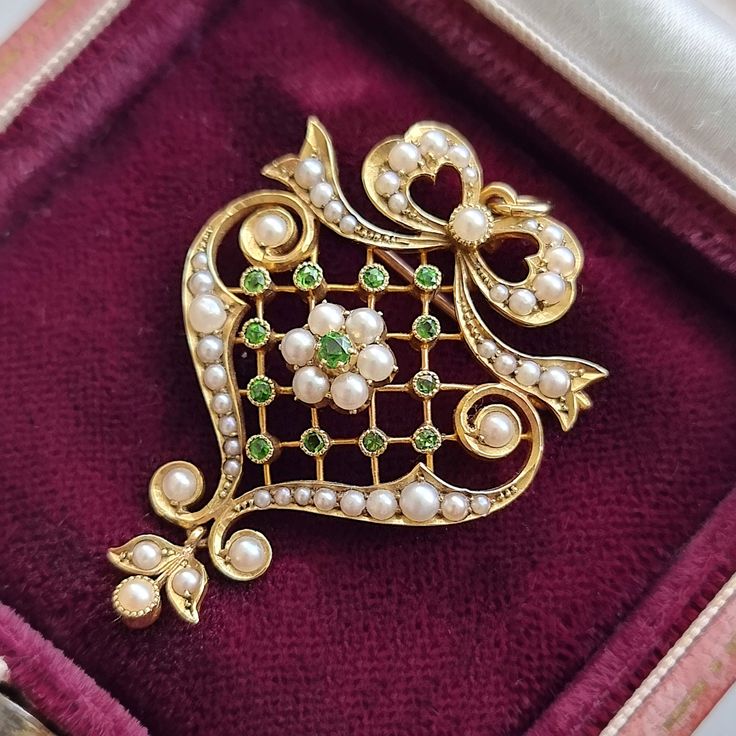 A stunning Edwardian pendant featuring demantoid garnets and seed pearls in a latticed body, with bow and leaf motifs, crafted in 15ct yellow gold, with a brooch and a pendant loop to the reverse. Circa 1900-1910. Stamped and tested as 15ct gold. The pendant measures approximately 41.5mm (L) x 27.9mm (W). The approximate weight is 6.3 grams. Please note that the chain and antique box pictured are for display purposes only. Thank you. CONDITION: In very good antique condition with some light surf Victorian Baroque Brooches As Gifts, Art Nouveau Wedding Brooches With Filigree, Antique Green Brooch For Anniversary, Antique Green Brooches For Anniversary, Green Art Nouveau Wedding Brooches, Antique Green Pendant Brooch, Elegant Brooches With Intricate Design For Gift, Art Deco Green Brooches For Wedding, Elegant Green Filigree Brooches