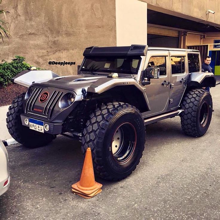 a gray jeep parked in front of a building with an orange cone on the ground