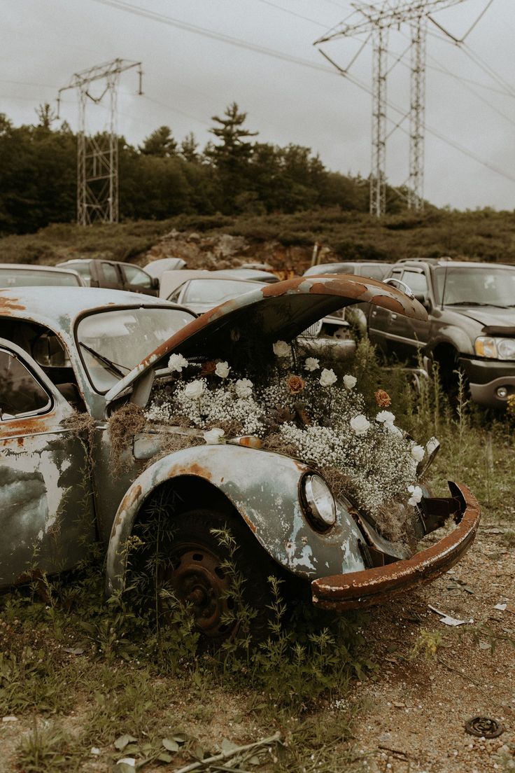 an old rusted out car sitting in the middle of a field with flowers growing out of it