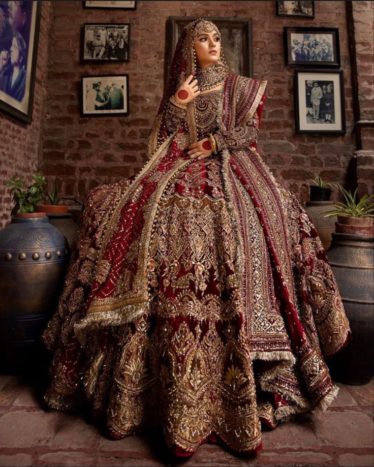 a woman in a red and gold bridal gown standing next to a brick wall