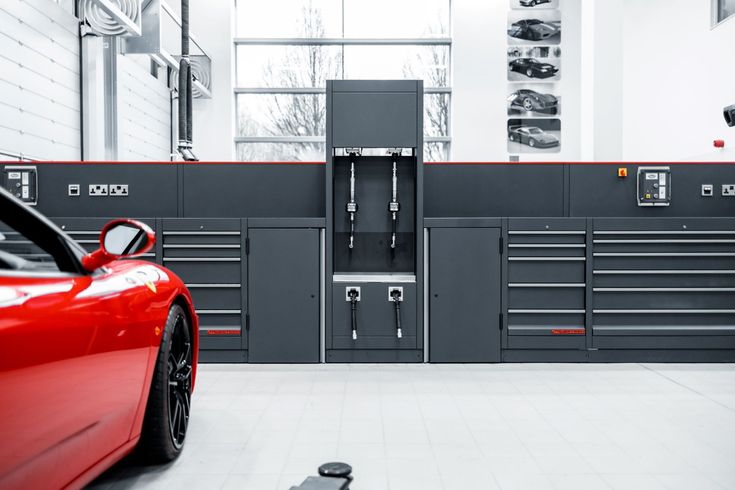 a red sports car parked in front of a garage with lots of work tools on the wall