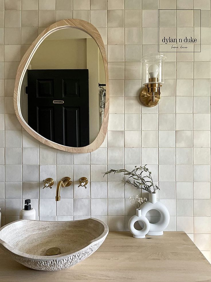 a bathroom sink sitting under a round mirror next to a vase with flowers in it