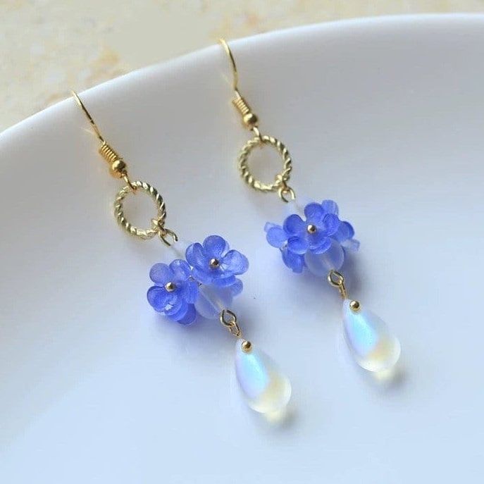 "Embrace the timeless beauty of these handmade earrings adorned with delicate little blue \"Forget Me Not\" flowers, symbolizing love and fidelity.  Suspended from each blossom, glistening crystal drops add a touch of sparkle and allure. With their understated charm and handmade craftsmanship, they make a captivating addition to any ensemble, infusing it with grace and romance. A perfect gift for her, these earrings exude elegance, making them an exquisite choice for bridal wear or as a captivat Jocelyn Core, Blue Forget Me Not Flowers, Beads Projects, Forget Me Not Flowers, Earring Ideas, Shrink Plastic, Beading Wire, Dangling Earrings, Crystal Drop