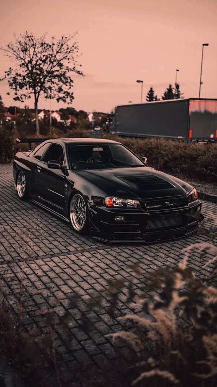 a black car parked on top of a brick road next to tall grass and trees