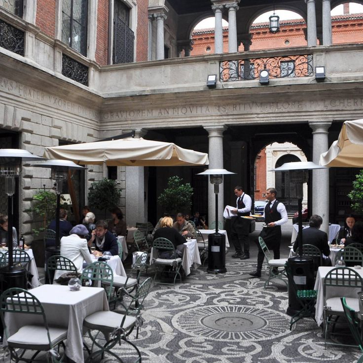 people are sitting at tables in an old building with white tablecloths and umbrellas