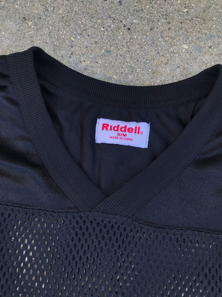 "Rock this amazing vintage black mesh jersey with a bold black leather pencil skirt. 100% Polyester Features modern aesthetic Brand: Riddell Estimate Size: M/L Listed Size: S/M Length: 24\" Bust: 46\" Waist: 46\"" 90s Black Stretch T-shirt, 90s Style Stretch Black T-shirt, Black Stretch 90s Style T-shirt, Black Stretch 90s Tops, Black Stretch 90s Style Tops, 90s Style Black Stretch Tops, Black Sporty Top With Mesh Sleeves, Sporty Black Top With Mesh Sleeves, 90s Style Black Tops For Fall