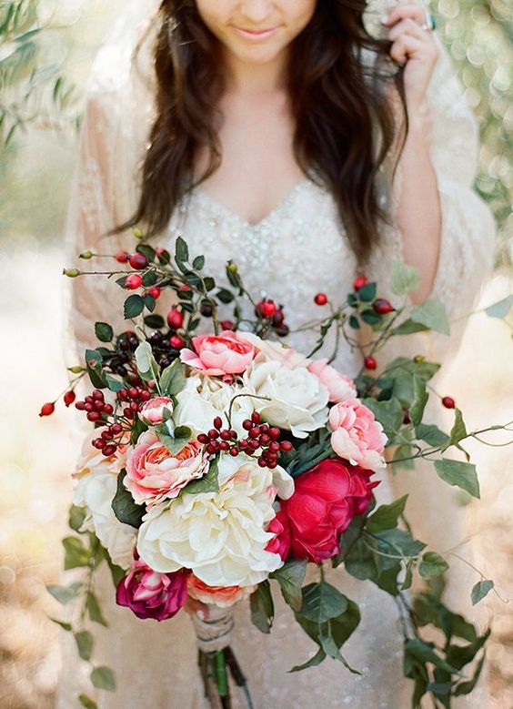 a woman holding a bouquet of flowers and greenery in front of her face while standing under an olive tree