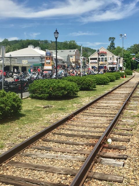 a train track with many cars parked on the other side and people walking down it