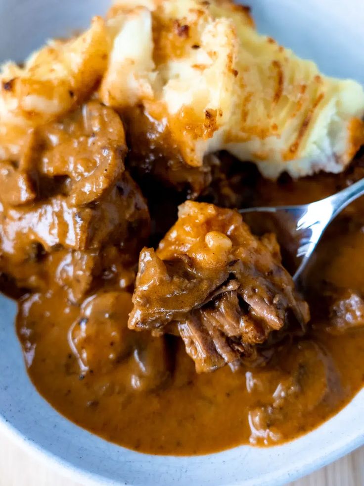 a white bowl filled with meat and gravy on top of a wooden table