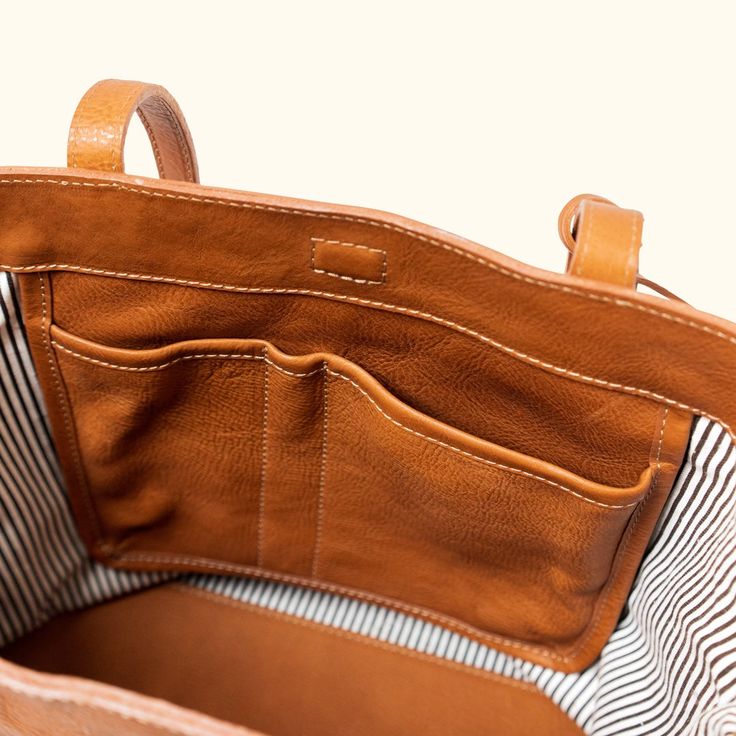 **Backordered - Expected Restock and Shipping Date May 6, 2022** The Madison saddle tan leather tote bag is crafted with gorgeous full-grain leather in a rich saddle tan finish. The stitching detail on the exterior brings attention to the tote’s fine craftsmanship, and the interior is thoughtfully lined with a neutral brown and white striped fabric. A tan leather tote bag is stylish and practical all year round, no matter the season or outfit. This particular tote is designed with multiple inter Tote Bag Pattern Leather, Tote Bag Straps, Buffalo Jackson, Mom Apparel, Tan Leather Tote, Boho Tote Bag, Leather Tote Bag Women, Everyday Hacks, Closet Essentials