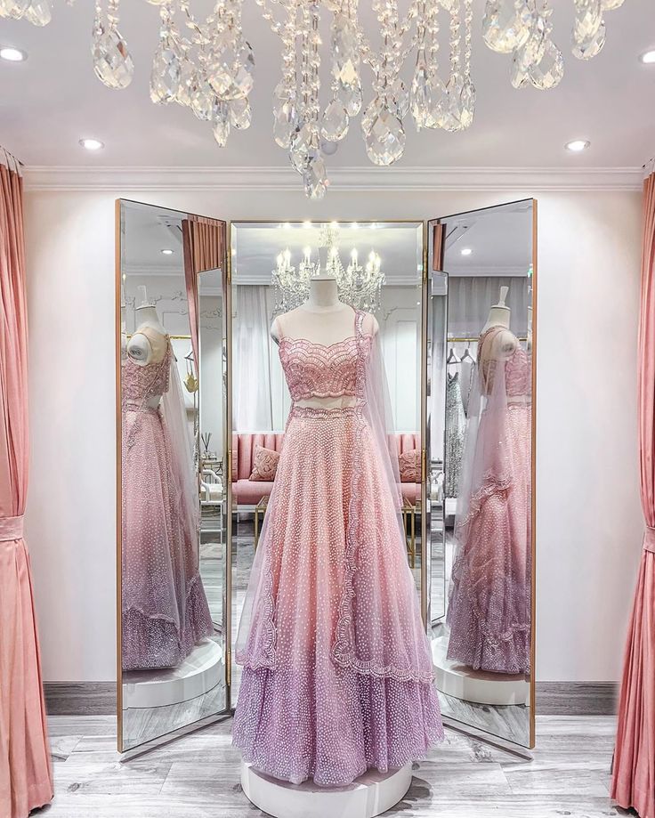 a dress on display in front of a mirror with pink curtains and chandelier