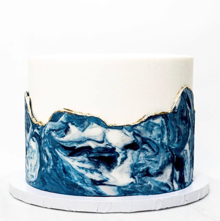 a blue and white marble cake with gold foiling on the top, sitting on a plate