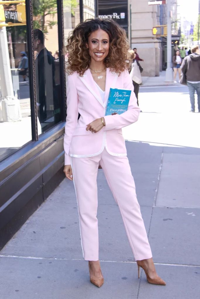 a woman in a pink suit is standing on the sidewalk