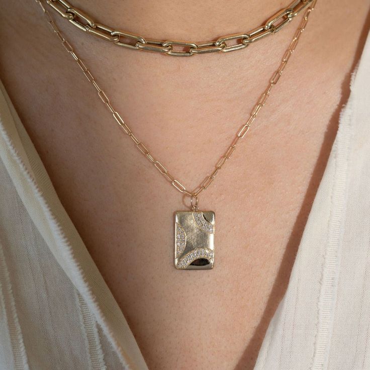 The 14k gold CAVE is a medium rectangular pendant with the signature JB brushed satin with shiny accents on the edge. The three sparkling rainbows of white diamonds highlight the piece. Available as pendant only, or with our recommended chain. Additional chain options available in our Chains & Chokers collection. Chain shown is 14k gold 1.8mm diamond cut ball chain Recommended chain lengths are 16" or 18" Full cut round white diamonds, approx .31ctw Dimensions are approximately 20mm x 14mm Desig Fine Jewelry Everyday Rectangular Pendant, Everyday Fine Jewelry With Rectangular Pendant, Gold Jewelry With Rectangular Polished Stone, Gold Jewelry With Polished Finish And Rectangular Stone, Rectangular Diamond Jewelry For Everyday Luxury, Everyday Luxury Rectangular Diamond Jewelry, Elegant Rectangular Charms Jewelry, Elegant Hammered Square Pendant Jewelry, Rectangular Gold Jewelry With Diamond Accents