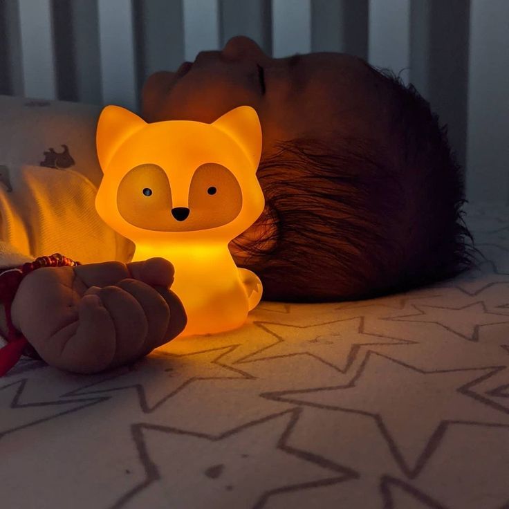 a baby laying in bed next to a lamp that looks like a fox