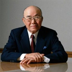 an older man in a suit and tie sitting at a table with his arms crossed