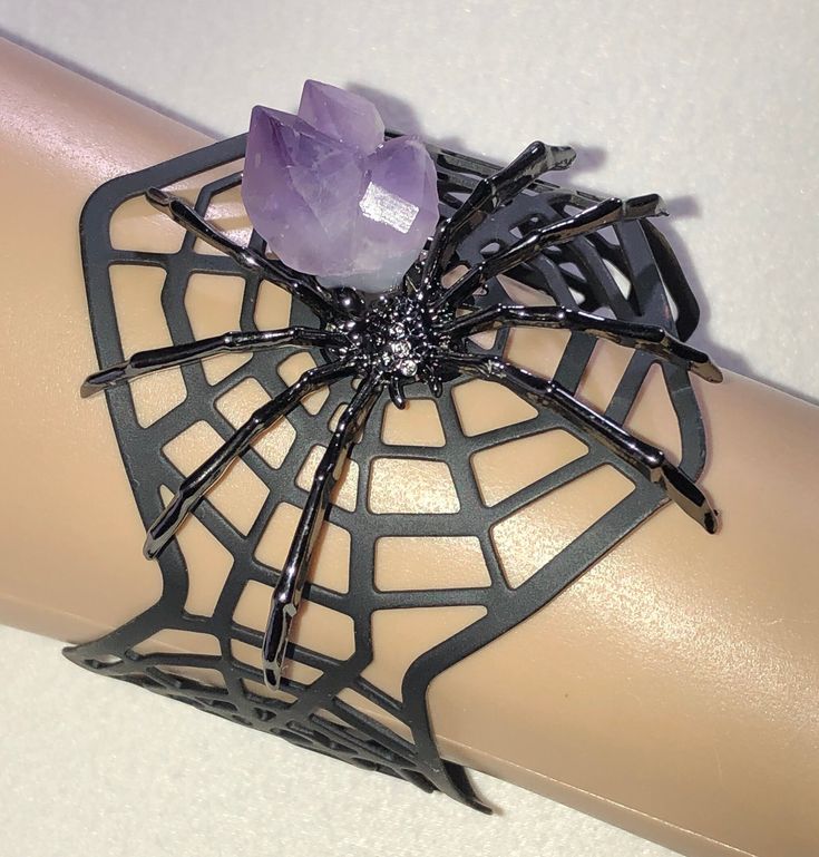 This bracelet is a one of a kind piece of art. The bracelet is matte black and lightweight. It bends and adjusts easily. The spider is shiny enamel with a natural amethyst crystal. I have one of these.  This item is a one of a kind so I'm not accepting returns but, if you get it and are not happy, let me know and I'll accept the return. I'm just trying to keep the costs down so I can sell items at low prices. My name is Malena. I sell vintage, upcycled/recycled and one of a kind jewelry. Everyth Spooky Adjustable Black Jewelry, Adjustable Black Spooky Jewelry, Gothic Bracelets For Halloween Gift, Gothic Halloween Bracelets As A Gift, Gothic Halloween Bracelets Gift, Gothic Adjustable Bracelets For Halloween, Black Spooky Jewelry For Party, Spooky Black Jewelry For Party, Spooky Black Jewelry For Halloween