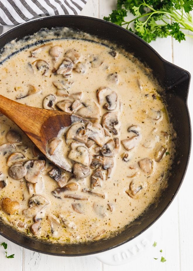 a skillet filled with mushroom soup on top of a white wooden table next to parsley