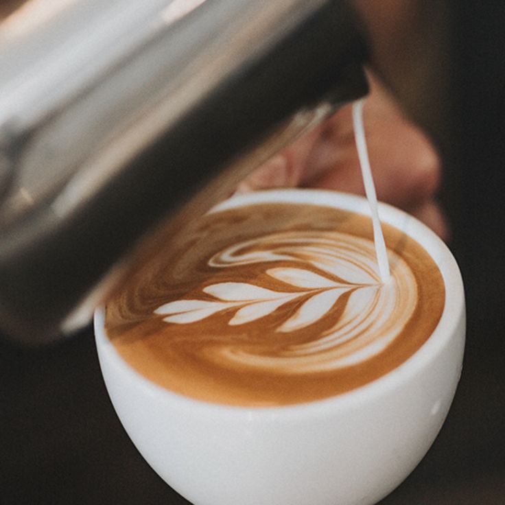 a person pouring coffee into a white cup