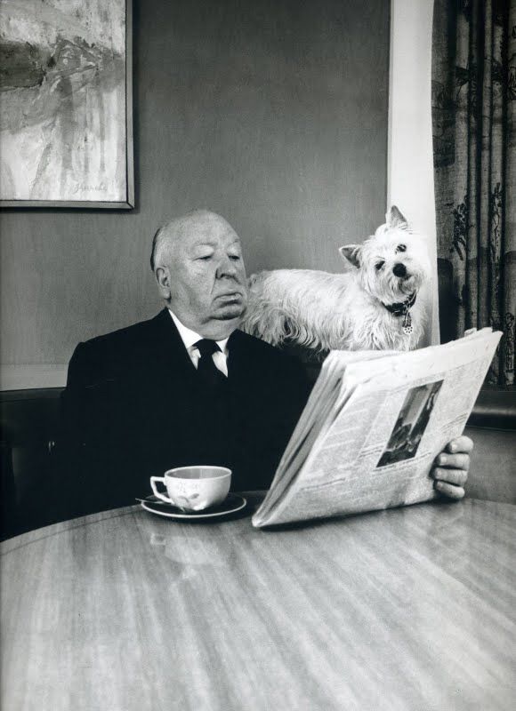 a man sitting at a table reading a newspaper with a dog standing on his back