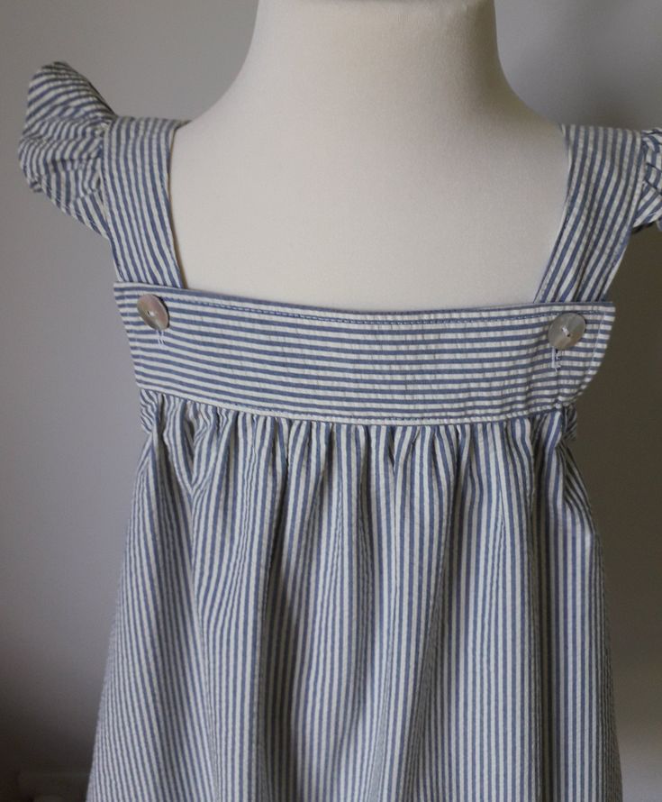 Striped seersucker sun dress with flared shoulder straps. This garment has a square neckline. The straps are fastened at the neckline with pearl buttons and the skirt is softly gathered from the yoke. It can be worn as a sundress or with a short or three quarter sleeve t shirt for cooler days. Size 4 to 5 years Approximate measurements. Length from shoulder 67 cm. Chest size 49cm. Cotton Smocked Sundress With Ruffled Straps, Summer Smocked Cotton Dress With Adjustable Straps, Cotton Sundress With Smocked Ruffled Straps, Cotton Smocked Dress With Square Neck For Beach, Cotton Sundress With Tie Back And Ruffled Straps, Cotton Sundress With Smocked Bodice And Square Neck, Cotton Smocked Dress With Square Neck, Cotton Square Neck Sundress With Smocked Back, Cute Smocked Summer Dress For Daywear