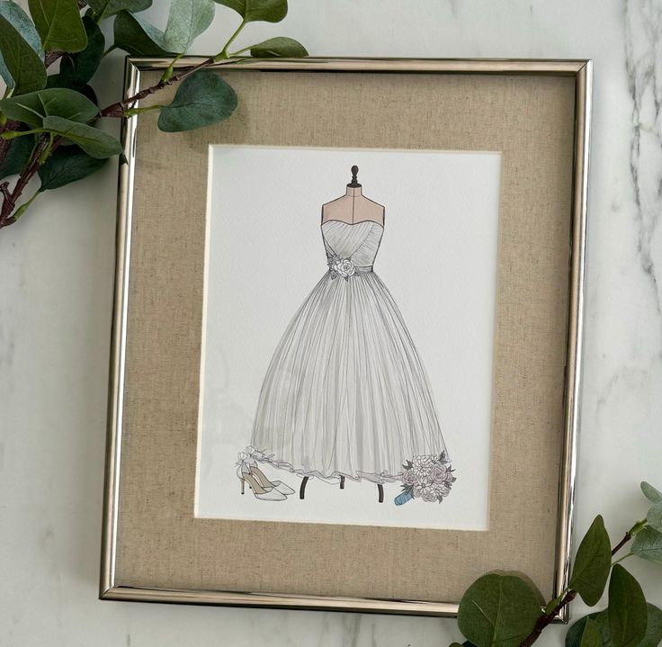 a drawing of a wedding dress is displayed in a frame on a marble countertop