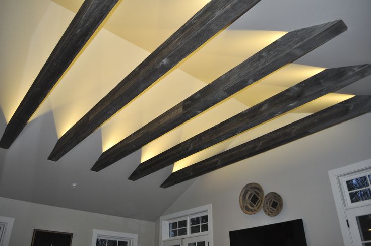 a living room with white walls and wooden beams on the ceiling is lit by recessed lights