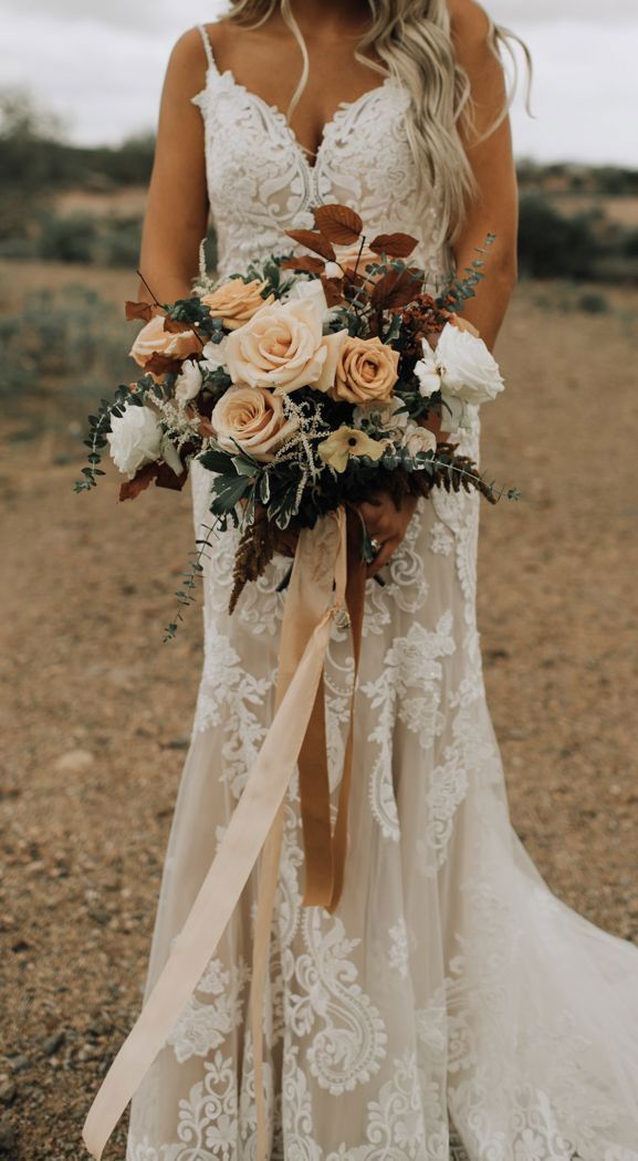 a woman in a wedding dress holding a bridal bouquet with roses and greenery