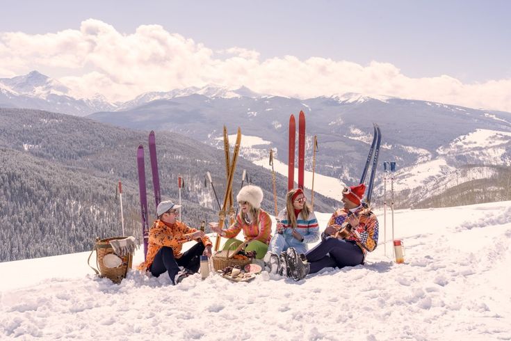 four skiers sitting in the snow with their skis and poles on top of a mountain